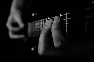 Close-up of hand playing guitar against black background