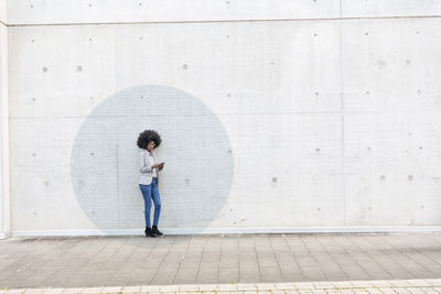 Full length of woman standing on footpath against wall