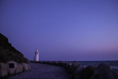 Lighthouse by sea against clear blue sky