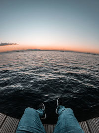 Low section of people relaxing by sea against sky during sunset
