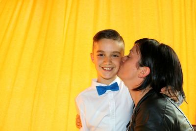 Side view of woman kissing son against yellow curtain