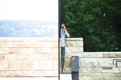 Reflection of man photographing in mirror against sky