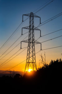 Low angle view of silhouette electricity pylons against sky during sunset