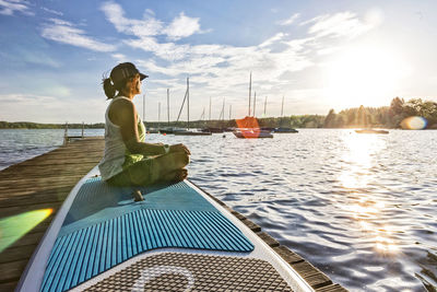 Woman sitting on boat by river against sky