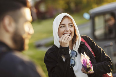 Cheerful young woman eating by man while looking away