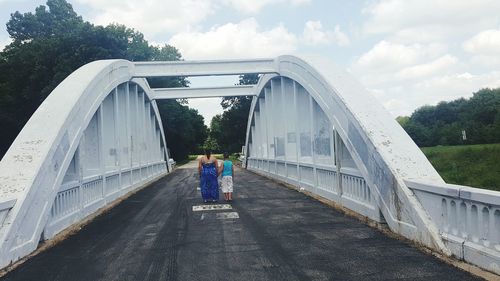 Rear view of people standing on road by bridge against sky