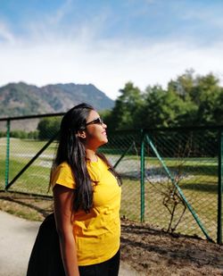 Side view of young woman looking away against sky