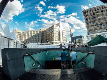 Rear view of people walking on subway staircase in city against sky