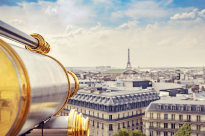 Close-up of hand-held telescope against buildings and distant eiffel tower