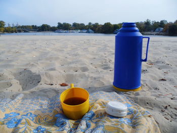 Water bottle on sand at beach against blue sky