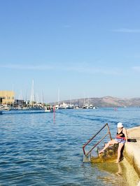 Full length of woman sitting by sea against sky during summer