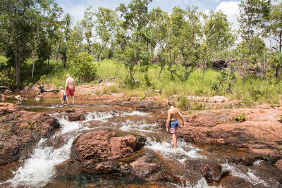 Shirtless people walking on rocks in river