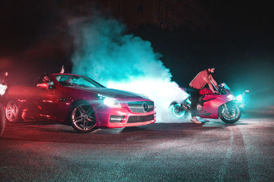 Man sitting on illuminated car at night