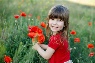 Portrait of happy girl with red flower in field