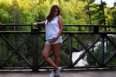 Portrait of beautiful woman standing by railing against trees