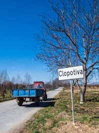 Information sign on road by trees on field against blue sky