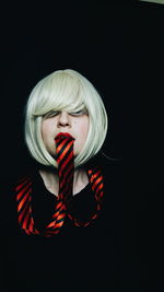 Portrait of mid adult woman with tie in mouth against black background