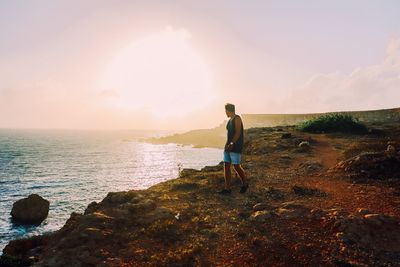 Man walking on shore against sea during sunset