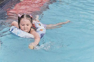 Happy adorable asian little girl swims in inflatable circle, having fun in open air thermal pool.