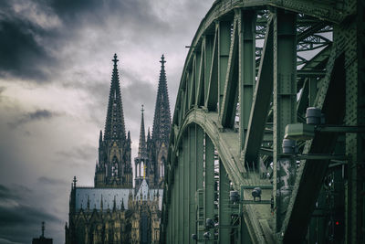 Low angle view of bridge and buildings against cloudy sky