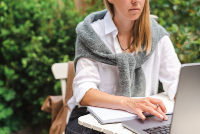 A woman takes notes in front of a laptop during an online business meeting outside.