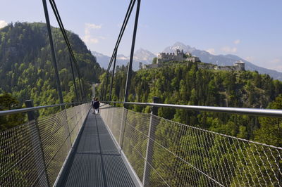 People on footbridge over trees against sky