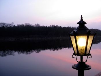 Illuminated lamp by lake against sky