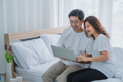 Young woman using mobile phone while sitting on bed at home