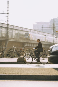 Male entrepreneur riding bicycle on road in city against sky