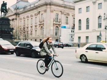 Woman riding bicycle on road against buildings in city