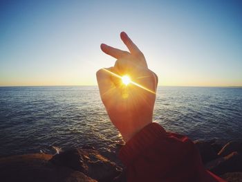 Close-up of hand holding sun at beach against sky during sunset