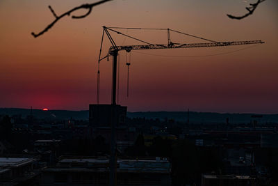 Silhouette cranes at construction site during sunset