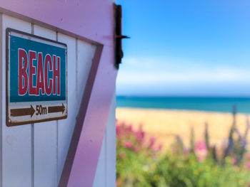 Close-up of sign board on beach against sky