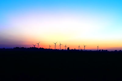 Silhouette of wind turbines on field against sky during sunset