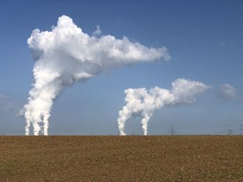 Smoke emitting from chimney on field against sky