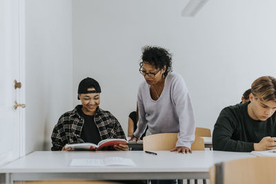 Teacher standing by smiling male student sitting at desk in classroom