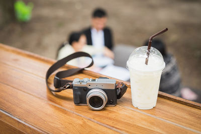 Close-up of camera and drink glass on table with people in background