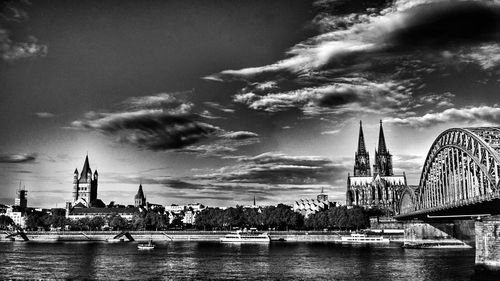 Bridge over river in city against cloudy sky