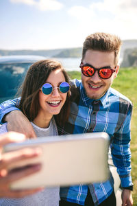 Young couple taking selfie while standing by car at beach