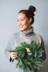 Adult woman with fir christmas wreath in hand on grey background