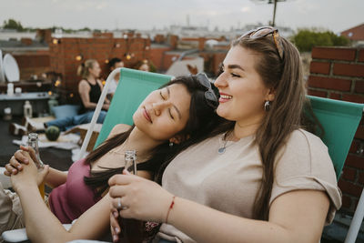 Young woman with eyes closed leaning on female friend holding beer bottle