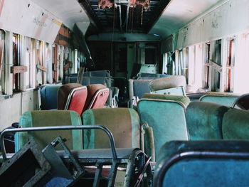 A jumble of old train seats sit in disarray in a decaying old passenger car.