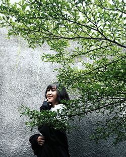 Young woman smiling while standing against tree