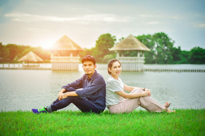 Portrait of smiling couple sitting on field by river