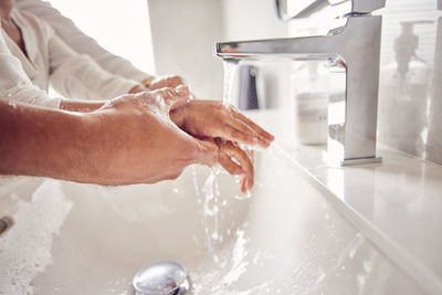 Cropped hand washing hands in bathroom