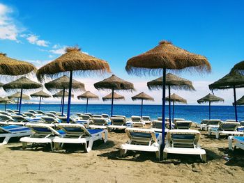 Lounge chairs and parasols on beach against blue sky