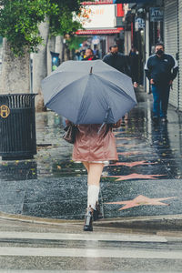 Attractive young woman walks down a rainy street with a plain black umbrella and a white skirt.