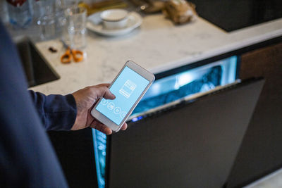 Cropped image of man using mobile app against dishwasher at smart home