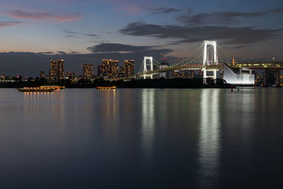 Illuminated city by river against sky at night