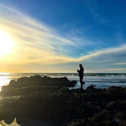 Silhouette man standing on beach against sky during sunset